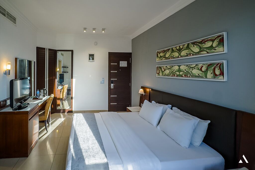 A hotel room with a bed, a desk with a TV, a chair, a wardrobe, and two wall-mounted artworks.