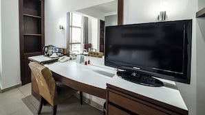 A hotel room with a large flat-screen TV, a desk with a telephone and a coffee maker, a chair, and a wardrobe. - Avenue Suites (Lagos)
