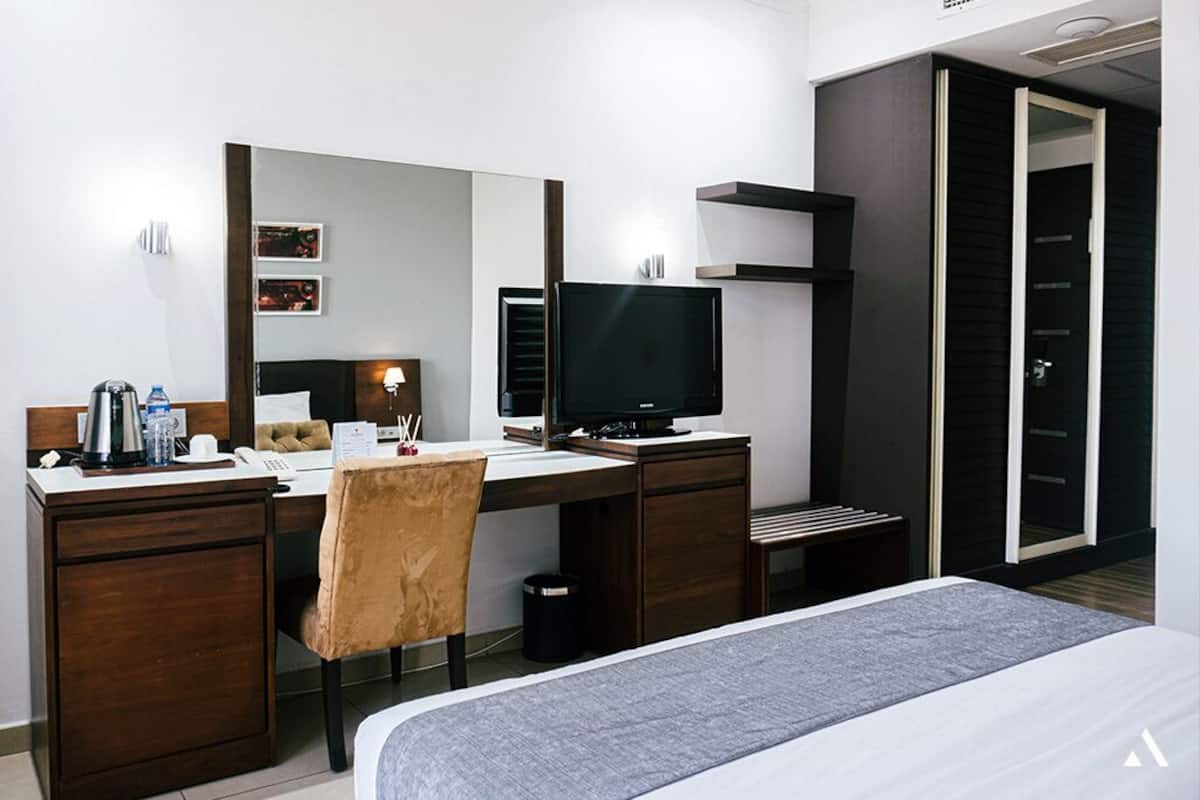 A modern hotel room with a bed, desk, chair, TV, and wardrobe.