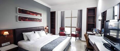 A hotel room with a large bed, a desk with a TV, a chair, and a window with curtains.