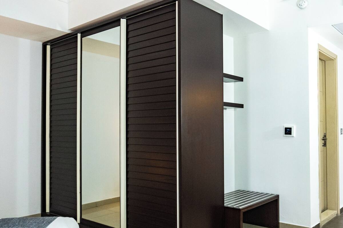 A modern bedroom with a large wardrobe, a bench, and a visible thermostat.