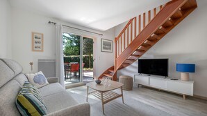 Een moderne woonkamer met een grijze bank, een houten salontafel, een televisie op een witte dressoir en een houten trap.