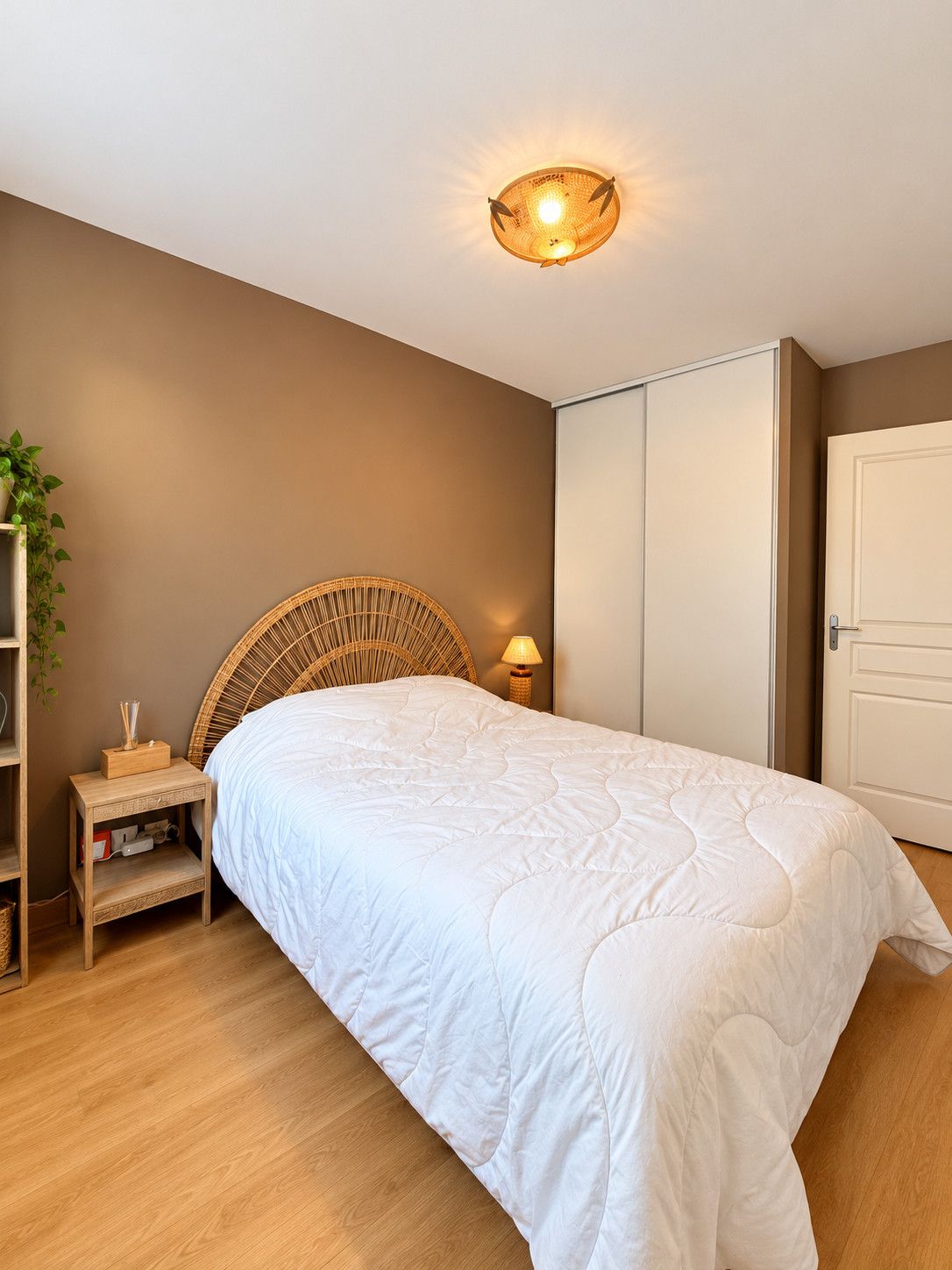 Een slaapkamer met een bed, nachtkastje, lamp, garderobe en een wandlamp.