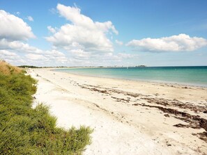 A wide sandy beach with gentle waves, a clear sky, and distant buildings. - House for 6 with garden, 900 m from the beach (Penmarch)