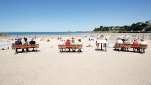 En strand med folk som sitter på bänkar, en klar himmel och ett lugnt hav.