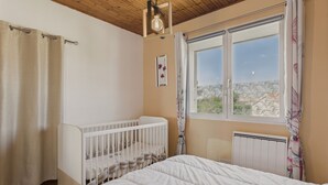 Una camera da letto con una culla, un'ampia finestra vista, un termosifone e un soffitto in legno.