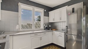 Una cucina moderna con mobili bianchi, un frigorifero in acciaio inossidabile e una finestra con vista sull'esterno.
