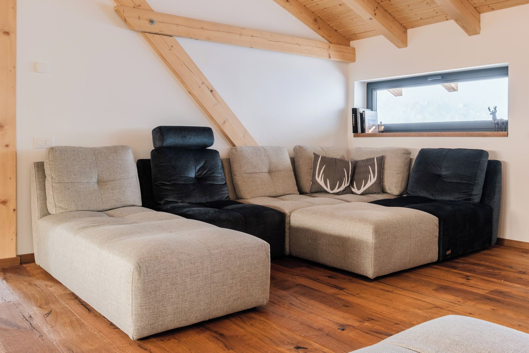 Un salon moderne avec un canapé d’angle, des poutres en bois, une fenêtre offrant une belle vue et un plancher en bois.