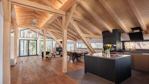A spacious loft with high ceilings, wooden beams, and large windows offering views of the outdoors.