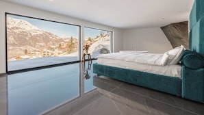A modern bedroom with a large bed, a view of a snowy mountain landscape, and a large window.