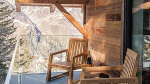 A wooden deck with two wooden chairs and a table, overlooking a mountainous landscape.