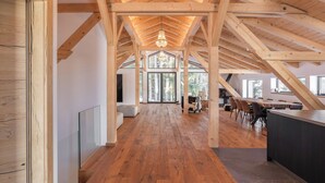 A spacious interior with a high wooden ceiling, a central chandelier, and a large dining area with a long table and chairs.