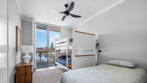 Une chambre avec un lit superposé, un ventilateur de plafond, une table de chevet avec une lampe et une vue sur l’extérieur.