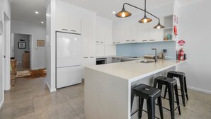 Une cuisine moderne avec des meubles blancs, un îlot central doté de tabourets et des luminaires suspendus.