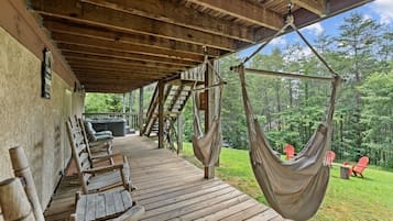 A wooden deck with a hammock, outdoor seating, and a hot tub.