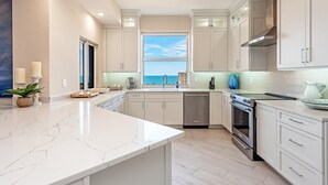 A modern kitchen with white cabinetry, a large island, and a view of the ocean. - Experience the Ultimate Vacation at Regatta! (Naples)