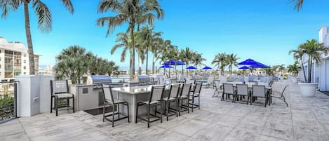 An outdoor patio with a grill, seating, and palm trees.