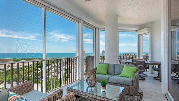 A spacious balcony with a glass table, wicker furniture, and a view of the ocean. - Experience the Ultimate Vacation at Regatta! (Naples)