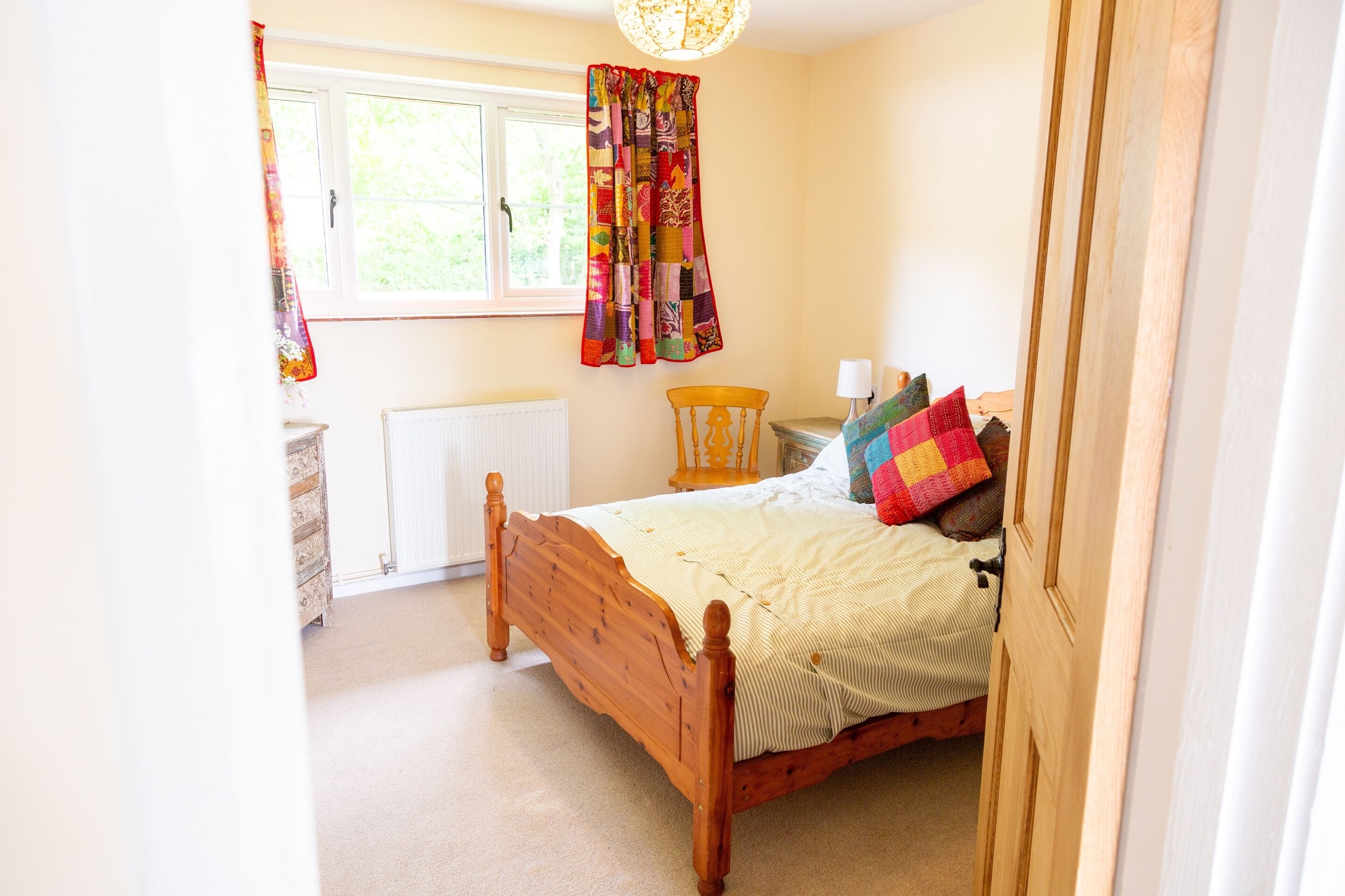 A bedroom with a wooden bed, a window with curtains, a radiator, and a chair.