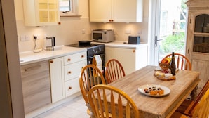 A modern kitchen with white cabinets, a wooden dining table, and four chairs. There are two pendant lights above the table. - 3 Bedroom idyllic countryside cottage in the middle of rural Wiltshire (Coate)
