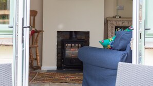 A cozy living room with a fireplace, a blue sofa, a wooden rocking chair, and a table with chairs. - 3 Bedroom idyllic countryside cottage in the middle of rural Wiltshire (Coate)