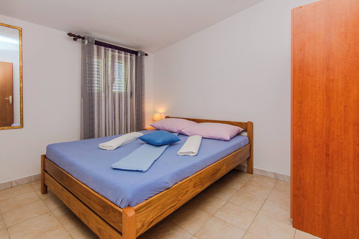 A single bed with a wooden frame, a blue mattress, and pillows in blue and pink.