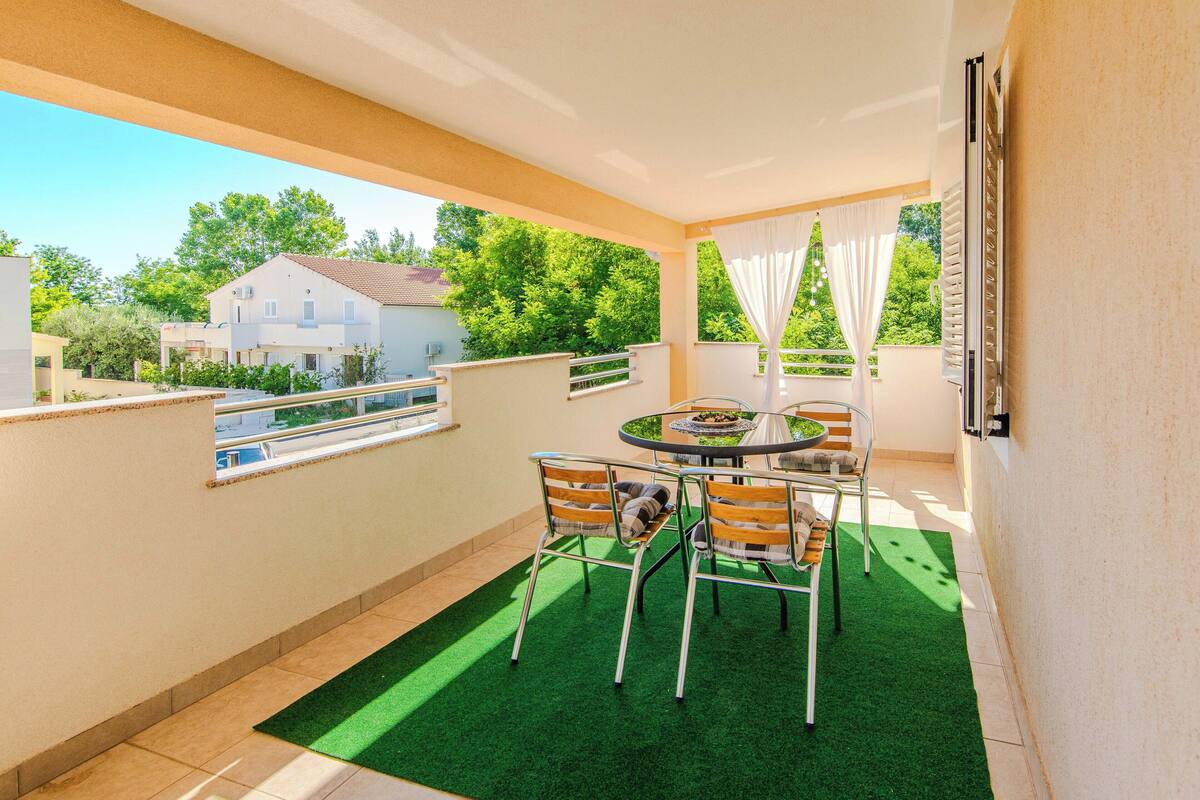 A balcony with a table and chairs, a view of a house, and a green artificial turf floor.