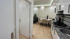 A modern kitchen with a dining area, featuring a white door, a dining table set with plates, and a stove. - Two-Bedroom Apartment in Taksim - No: 3 (İstanbul)