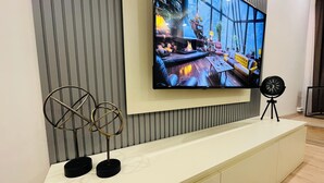 A modern living room with a large flat-screen TV mounted on a wall, a white entertainment unit below, and a small round table with a clock. - Two-Bedroom Apartment in Taksim - No: 3 (İstanbul)