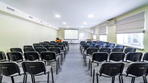Ein Konferenzraum mit Reihen von Stühlen, die auf eine Projektionsleinwand zeigen, einem Rednerpult und einer Whiteboard-Tafel.
