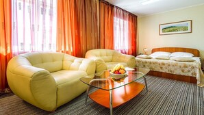 Ein Hotelzimmer mit einem Bett, zwei Sofas, einem Glastisch mit Früchten und Vorhängen.