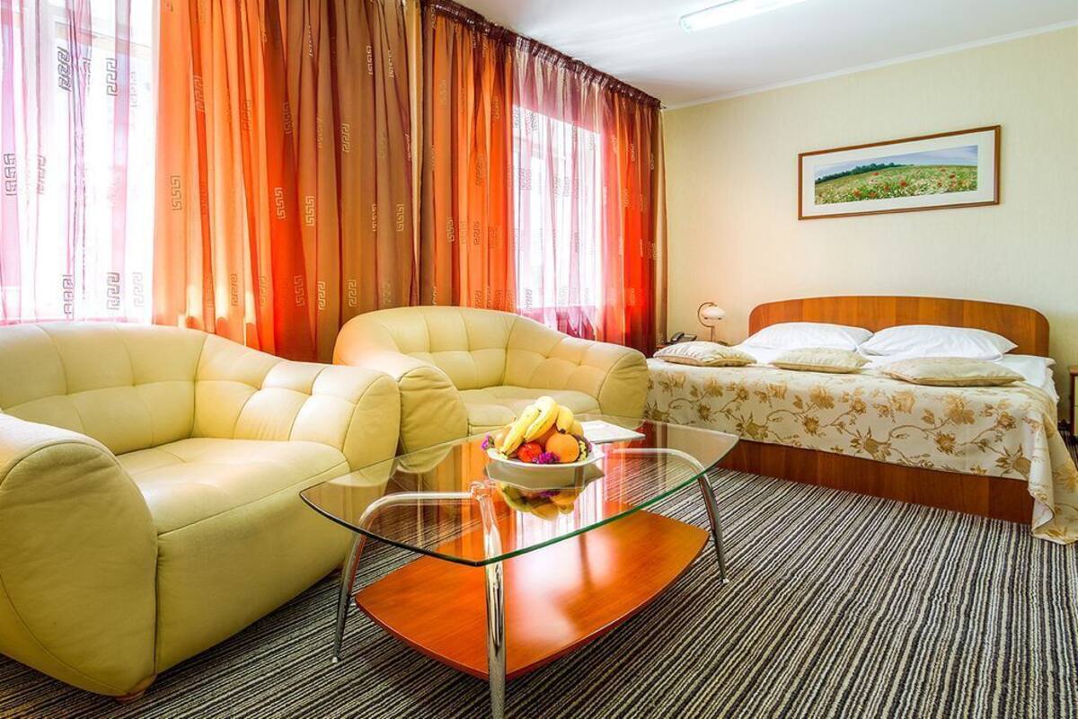 Ein Hotelzimmer mit einem Bett, zwei Sofas, einem Glastisch mit Früchten und Vorhängen.