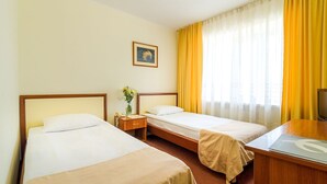 A hotel room with two beds, a desk, a chair, a TV, and a window with curtains.
