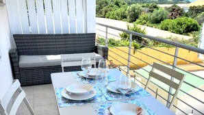 A dining area with a table set for four, white chairs, and a black sofa.