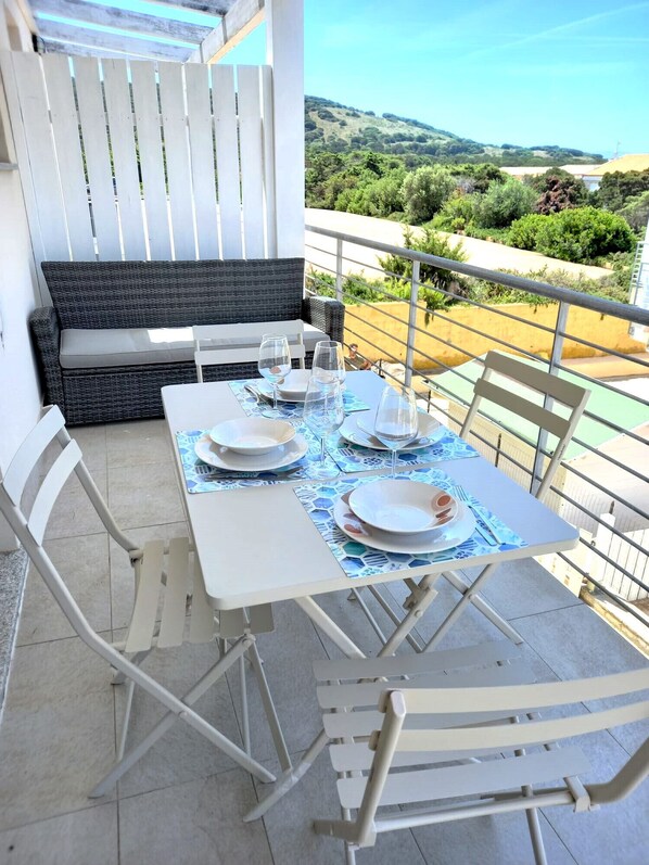 A dining area with a table set for four, white chairs, and a black sofa.