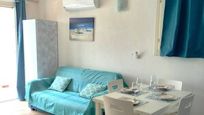 A room with a teal sofa, a white dining table with chairs, and a painting on the wall.