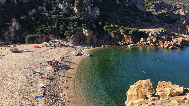A beach with clear water, rocky cliffs, and umbrellas.