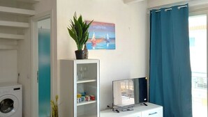 A modern living room with a flat-screen TV, a potted plant, and a painting on the wall.