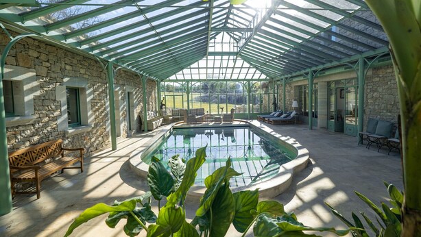 Un área de piscina al aire libre techada, con paredes de piedra, sillas de descanso y un banco.