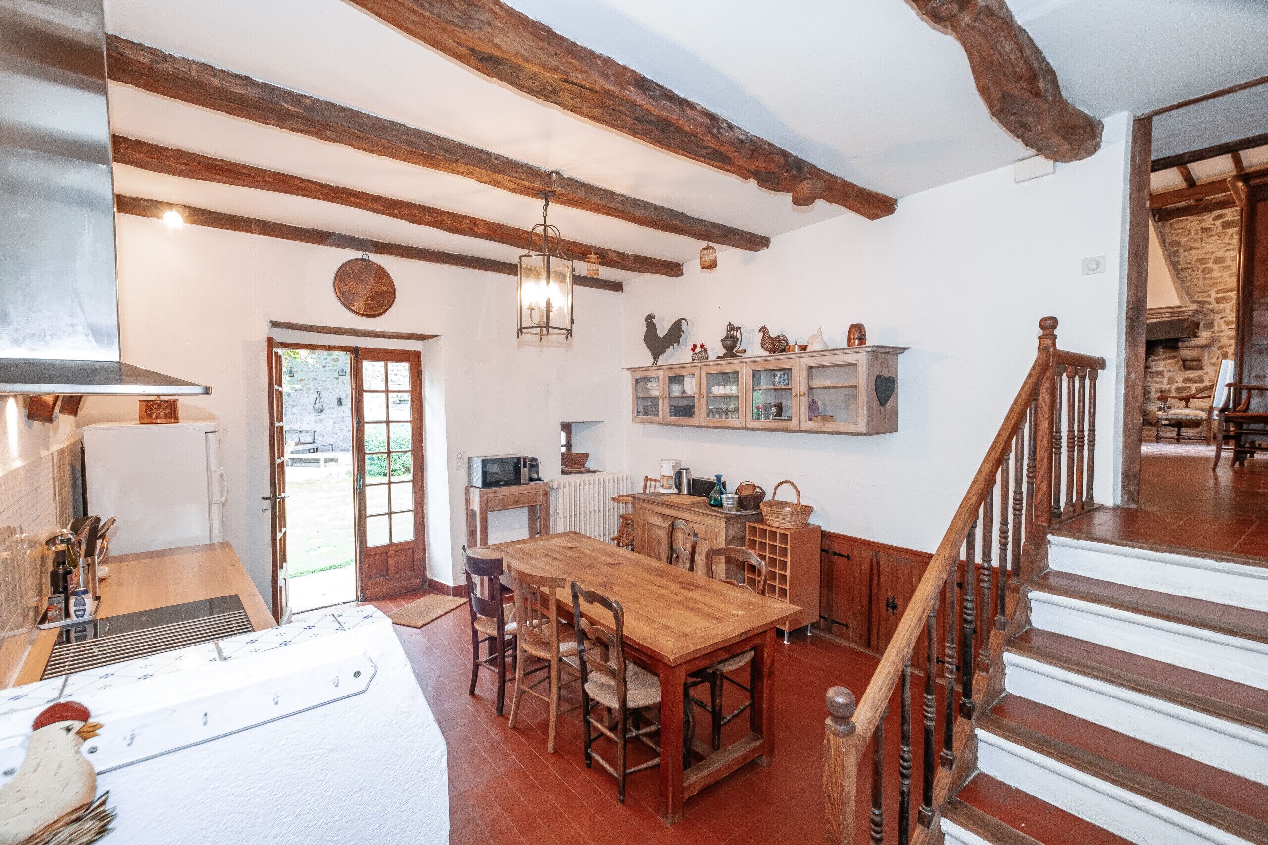 A rustic kitchen with wooden beams, a dining table, and a staircase leading to another room.