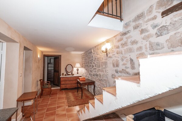 Una habitación con pared de piedra, escalera de madera, una mesa de comedor con sillas, una lámpara y un espejo.