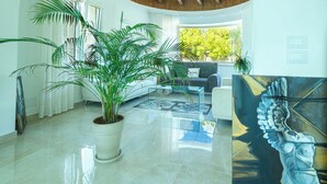 Een ruime woonkamer met een grote potplant, een glazen salontafel en een moderne bank.