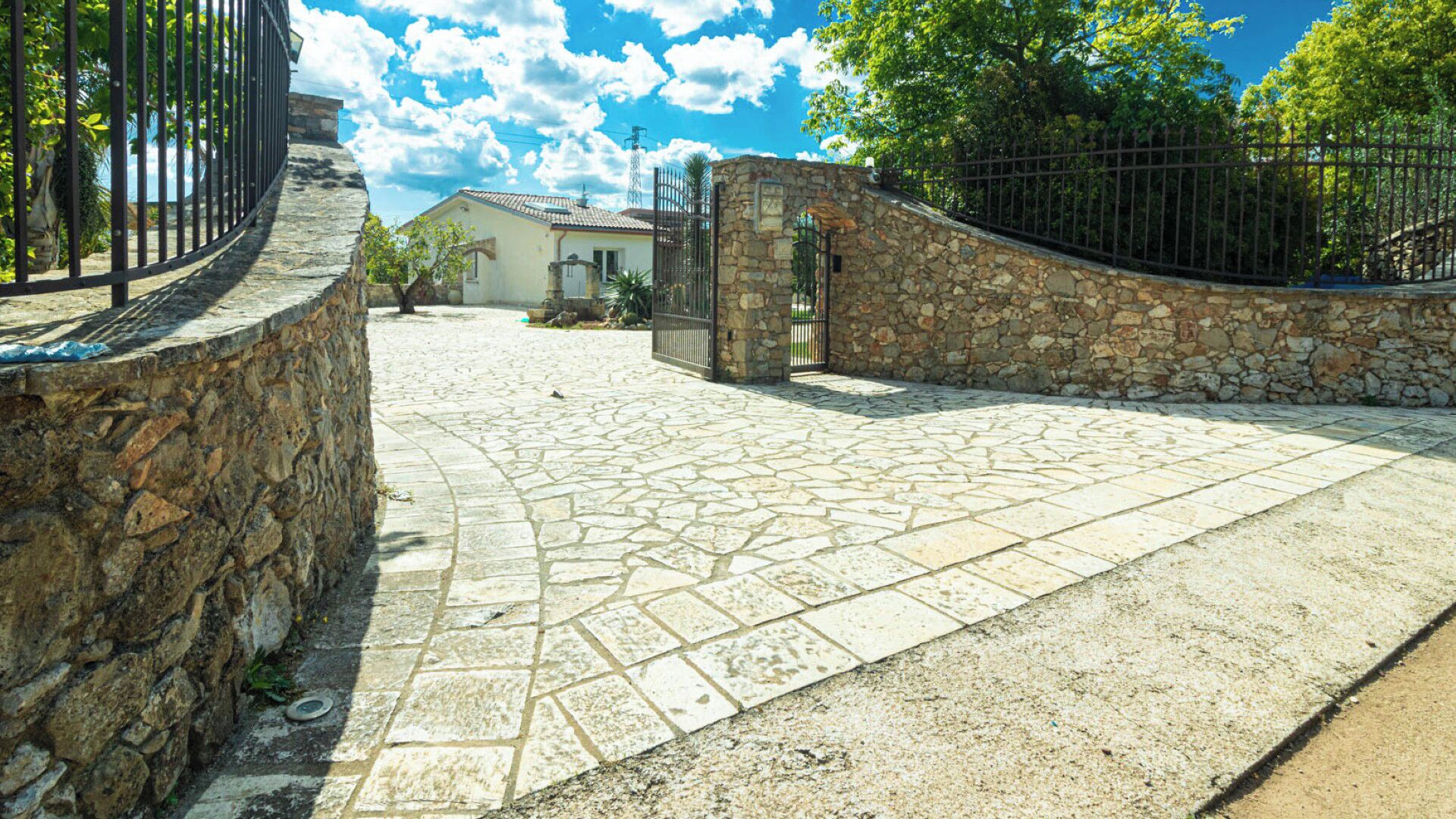 Un cortile lastricato con mura in pietra e un cancello in metallo.
