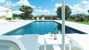 Piscina con sillas de descanso y una mesa con botella y vaso.