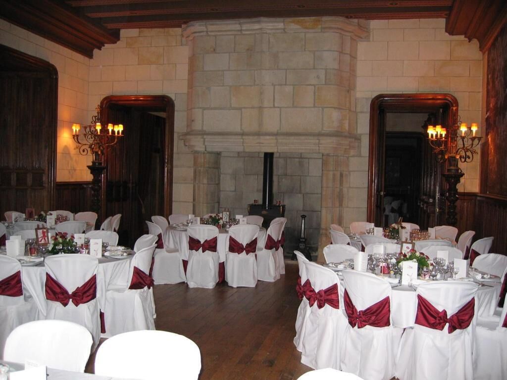 A banquet hall with round tables set for a formal event, featuring white tablecloths and red sashes.