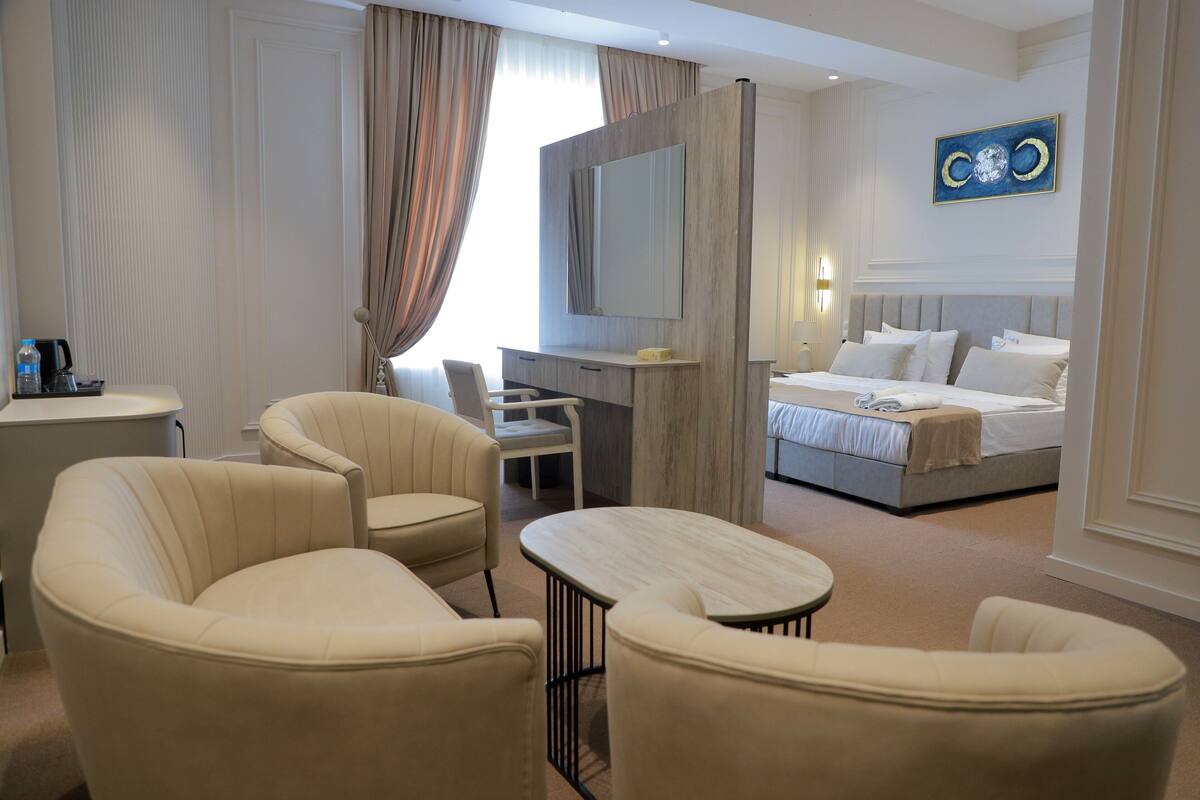 A hotel room with a bed, a desk, two chairs, a small table, and a TV.
