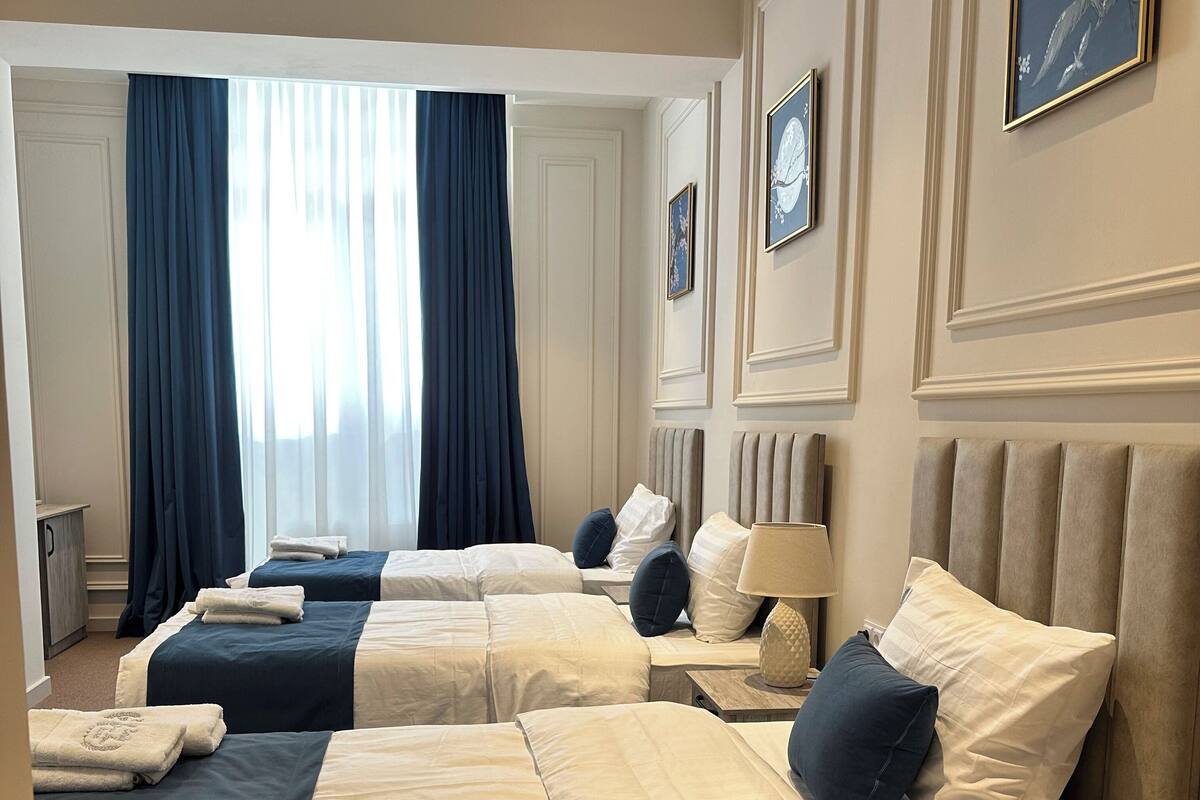A hotel room with three beds, each with a headboard, bedside tables, and a lamp.