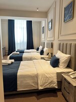 Quarto de hotel com três camas, cada uma com cabeceira, mesas de cabeceira e uma luminária.