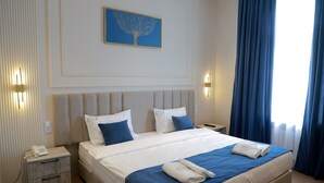 Hotellihuone, jossa on suuri sänky, kaksi yöpöytää, seinään kiinnitetty puhelin ja sängyn yläpuolella oleva taulu.