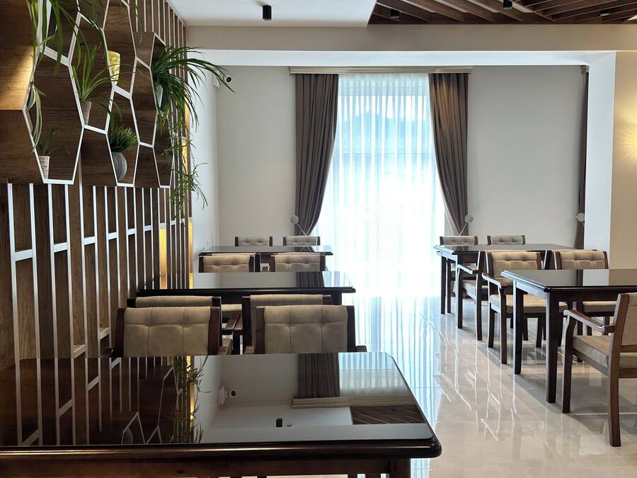 Un moderno vestíbulo de hotel con una mesa de centro de vidrio, sillones de cuero, una pared vegetal hexagonal y un gran ventanal con cortinas.